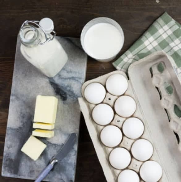 Milk, cream, sliced butter and a carton of fresh eggs on a marble board