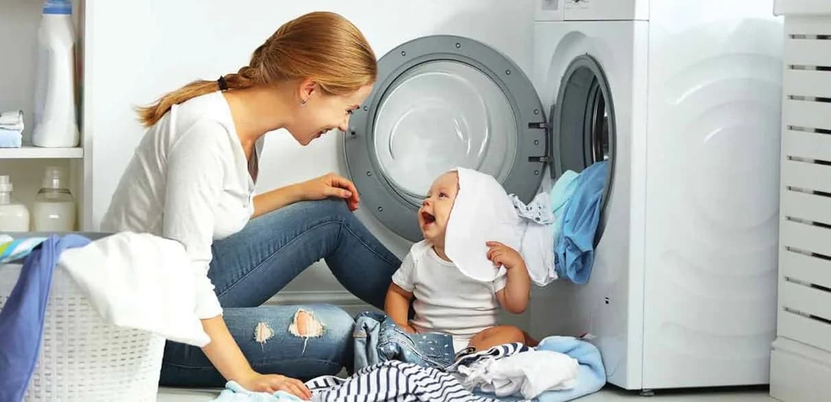 Mother and baby laughing together in front of a washing machine