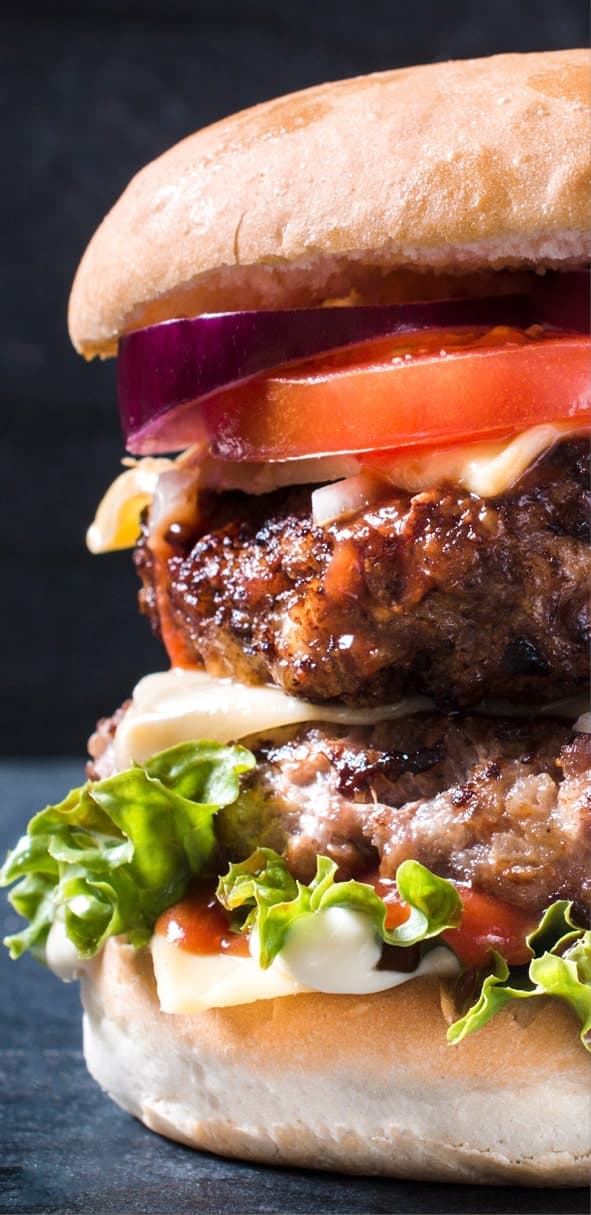 A stacked double cheeseburger with lettuce, tomato, and onion