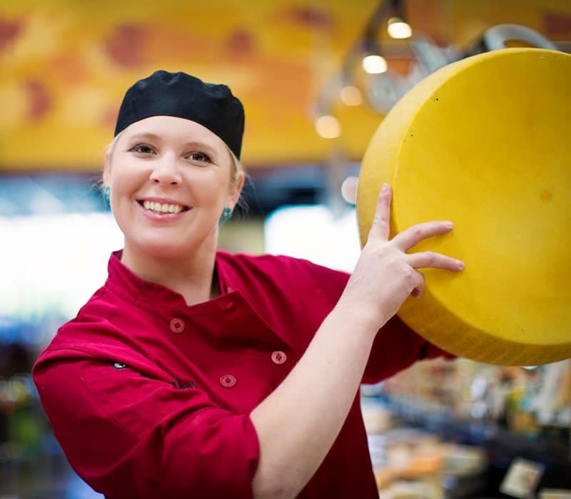 A Harmons associate holding a large wheel of cheese in the cheese department