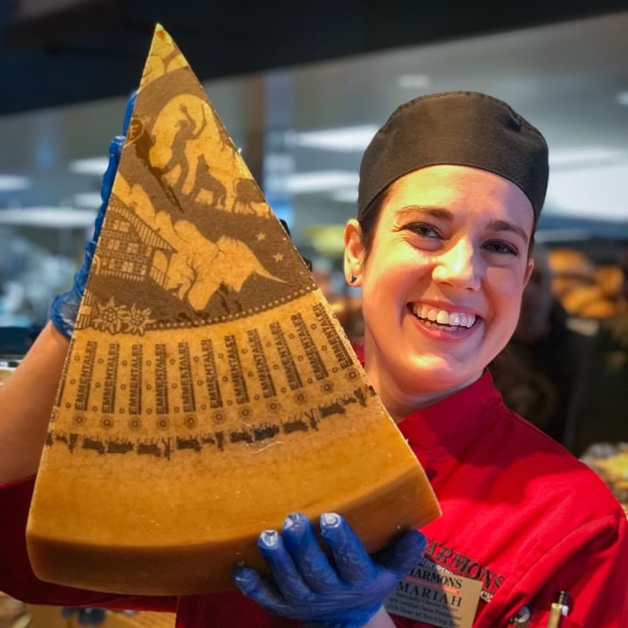 A Harmons cheesemonger smiling while holding a large wedge of Parmigiano cheese