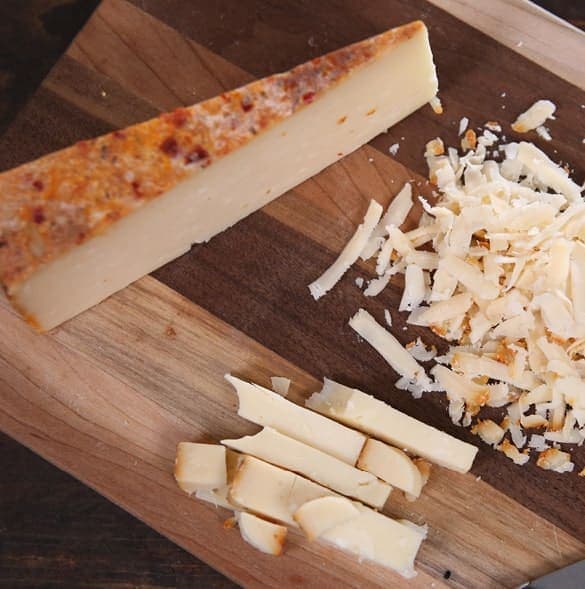 Assorted specialty cheeses sliced and shredded on a wooden cutting board